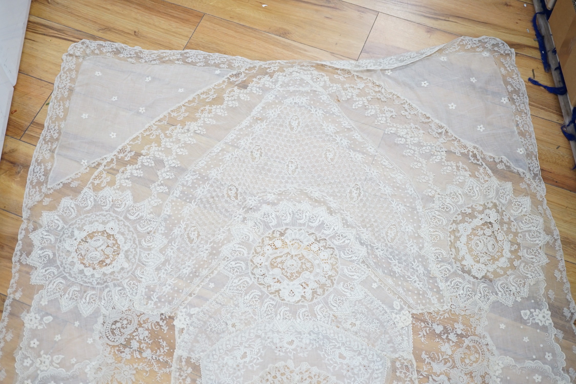 A late 19th century Normandy lace table cover of hand spun linen, hand white worked, with Brussels Point de Gaze insertions and bobbin lace edging, together with two feathers and a net veil